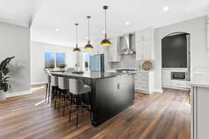 Kitchen featuring wall chimney exhaust hood, freestanding refrigerator, wood finished floors, a kitchen island, and arched walkways