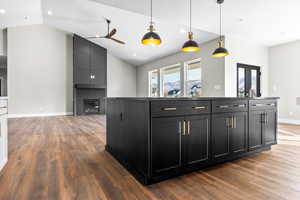 Kitchen featuring a large fireplace, wood finished floors, a ceiling fan, lofted ceiling, and dark cabinetry