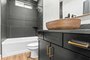 Bathroom with toilet, wood finished floors, and washtub / shower combination