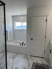 Bathroom with vanity, a garden tub, marble look tile flooring, and a textured ceiling