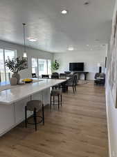 Kitchen featuring a textured ceiling, light wood finished floors, plenty of natural light, decorative light fixtures, and a breakfast bar area