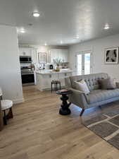 Living room featuring a textured ceiling, light wood finished floors, recessed lighting, and french doors