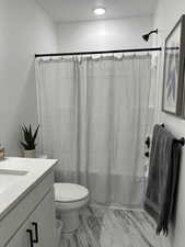 Bathroom with shower / bath combination with curtain, vanity, toilet, and marble finish flooring