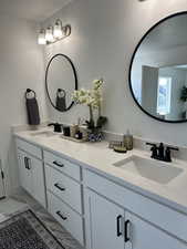 Full bath with double vanity, marble look tile flooring, and a textured ceiling