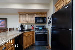Kitchen featuring black appliances, a sink, light stone countertops, brown cabinetry, and a peninsula