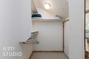 Spacious  walk- in closet featuring carpet flooring and vaulted ceiling