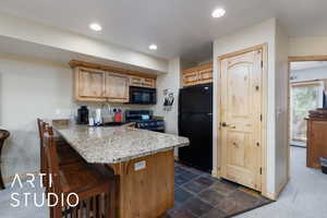 Kitchen featuring black appliances, a sink, a kitchen breakfast bar, baseboards, and a peninsula