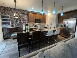 Kitchen with stainless steel refrigerator with ice dispenser, black microwave, wood finished floors, a center island with sink, and recessed lighting