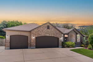 French country inspired facade with a garage, brick siding, driveway, and roof with shingles