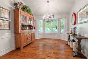 Formal dining room featuring bay window, chandelier,  hardwood flooring,  wainscoting, and lofted ceiling