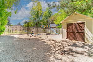 View of jungle gym featuring a fenced backyard and storage shed