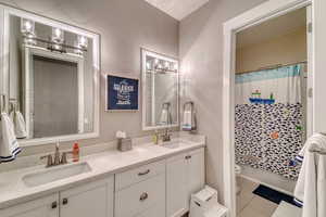 Bathroom with toilet, double vanity, tile patterned floors, and shower / tub combo with curtain