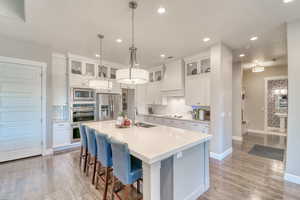 Kitchen featuring stainless steel appliances, a sink, premium range hood, decorative backsplash, and a center island with sink