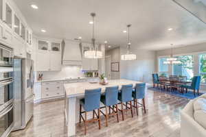 Kitchen with custom exhaust hood, appliances with stainless steel finishes, light countertops, light wood-type flooring, and a sink