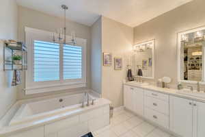 Bathroom featuring a chandelier, tile patterned flooring, double vanity, a garden tub, and a textured ceiling