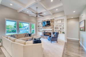 Living area featuring baseboards, a ceiling fan, light wood-type flooring, a stone fireplace, and coffered ceiling
