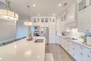 Kitchen featuring stainless steel appliances, a sink, premium range hood, light wood finished floors, and white cabinets