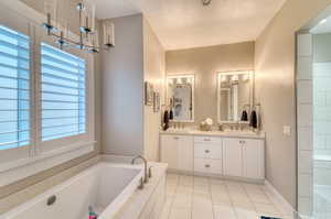 Full bath featuring a textured ceiling, double vanity, a bath, tile patterned floors, and plenty of natural light