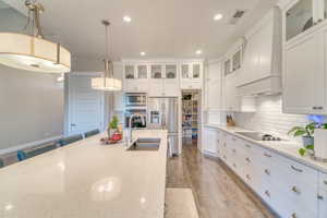 Kitchen featuring stainless steel appliances, a sink, premium range hood, light wood-style flooring, and decorative light fixtures