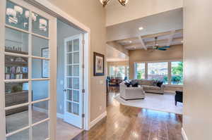 Hall featuring coffered ceiling, beam ceiling, hardwood / wood-style floors, baseboards, and a chandelier