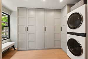 Washroom featuring stacked washing machine and dryer, light wood finished floors, and recessed lighting
