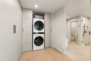 Washroom featuring stacked washer and clothes dryer, baseboards, recessed lighting, and light wood-style flooring