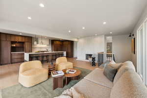 Living room with light wood-style flooring, recessed lighting, and bar with sink