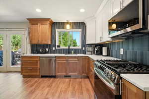 Kitchen with appliances with stainless steel finishes, a sink, light countertops, backsplash, and light wood-type flooring