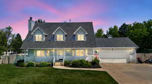 Cape cod home featuring a chimney, a garage, driveway, covered porch, and a shingled roof