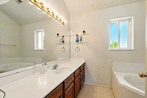 Full bathroom featuring vanity, a bath, baseboards, lofted ceiling, and tile patterned floors