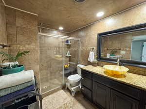Full bath featuring tile walls, vanity, a shower stall, toilet, and recessed lighting