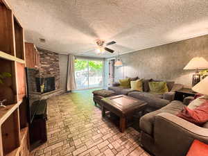 Living area featuring ceiling fan, brick patterned flooring, and a stone fireplace