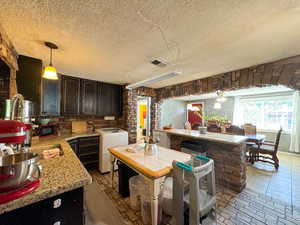 Kitchen with washer / dryer, dark brown cabinets, a textured ceiling, decorative light fixtures, and black microwave