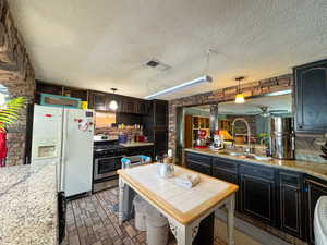 Kitchen featuring white fridge with ice dispenser, stainless steel gas range oven, a sink, brick patterned floors, and a textured ceiling