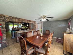 Dining room with a textured ceiling, a ceiling fan, light tile patterned flooring, and bar area