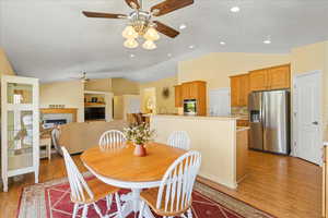 Dining area featuring ceiling fan, lofted ceiling, light wood finished floors, a glass covered fireplace, and recessed lighting