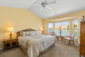Bedroom with vaulted ceiling, multiple windows, a water view, light colored carpet, and ceiling fan