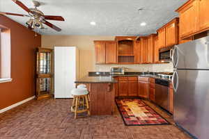 Kitchen featuring appliances with stainless steel finishes, open shelves, a kitchen breakfast bar, a ceiling fan, and a sink