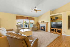 Living area featuring vaulted ceiling, a ceiling fan, light wood finished floors, a tile fireplace, and a textured ceiling
