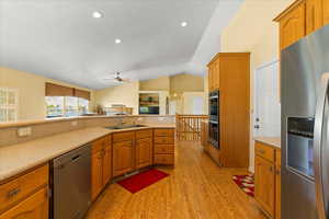 Kitchen featuring appliances with stainless steel finishes, a sink, light wood finished floors, ceiling fan, and lofted ceiling