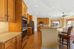 Kitchen featuring appliances with stainless steel finishes, a kitchen island with sink, brown cabinets, recessed lighting, and tasteful backsplash