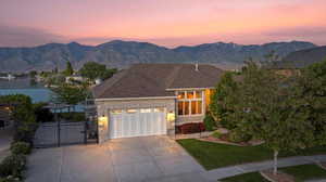 View of front facade featuring an attached garage, concrete driveway, a gate, a water and mountain view, and a shingled roof
