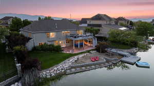 Back of house at dusk with a lawn, a deck with water view, a patio, and a residential view