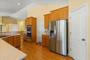 Kitchen with stainless steel appliances, vaulted ceiling, backsplash, light wood finished floors, and light countertops