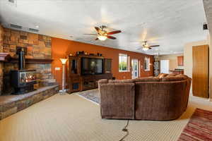 Living room featuring carpet, a ceiling fan, a textured ceiling, a wood stove, and baseboards