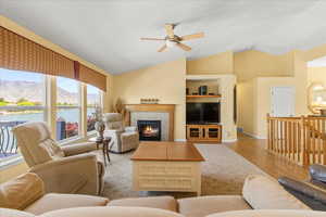 Living room with a ceiling fan, vaulted ceiling, a tiled fireplace, and wood finished floors