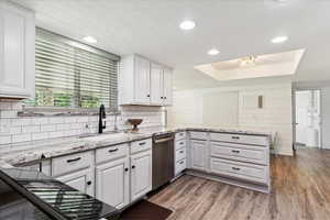 Kitchen featuring dishwasher, a sink, white cabinetry, a tray ceiling, and recessed lighting