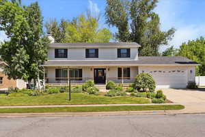 Traditional-style home featuring a garage, driveway, a chimney, a front yard, and covered porch
