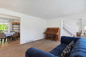 Living room with carpet, stairs, ornamental molding, crown molding, and tall colonial baseboards