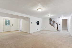 Finished basement den area featuring light carpet, a textured ceiling, stairway, and baseboards